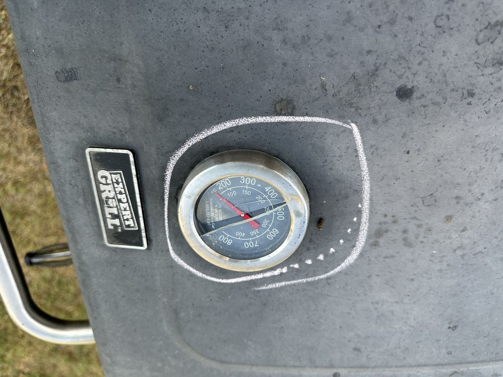 Hail dent circled in chalk on a grill thermometer gauge
