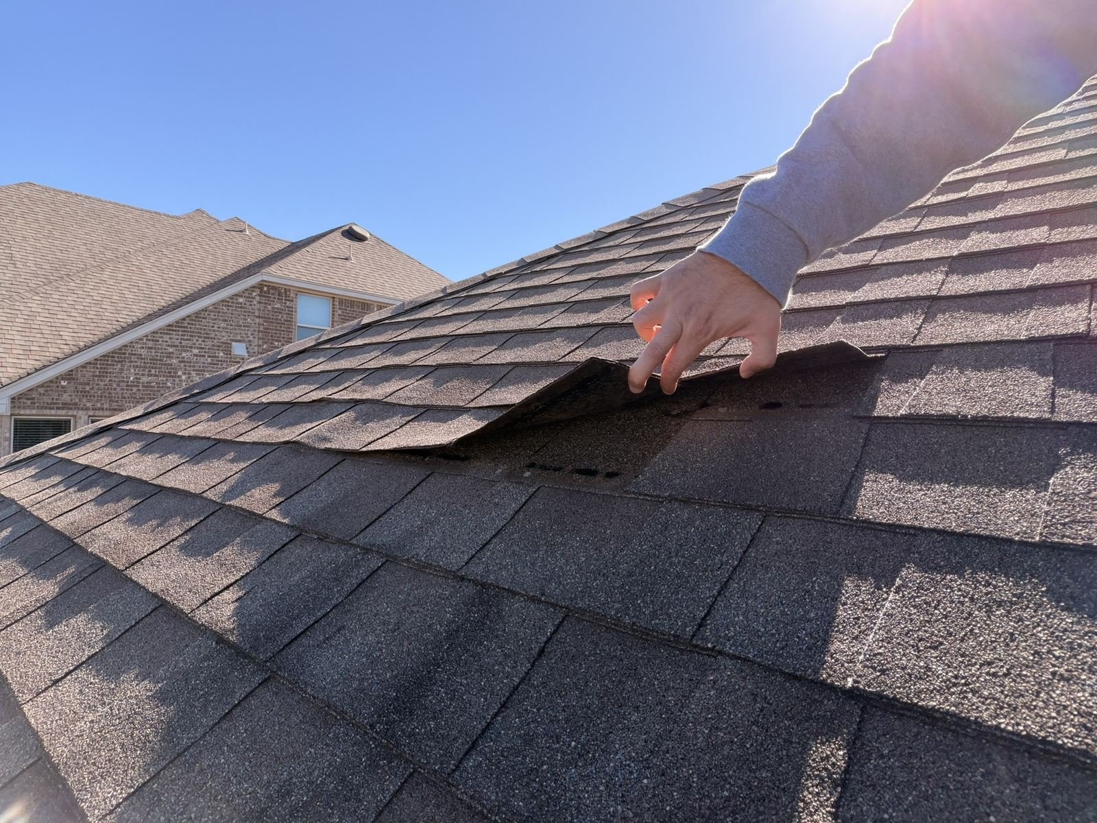 Wind-creased shingle lifted by hand to show the broken seal